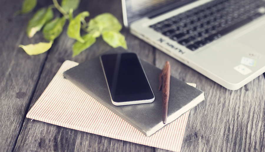 Smartphone, diary, pen and laptop on wooden table outdoor